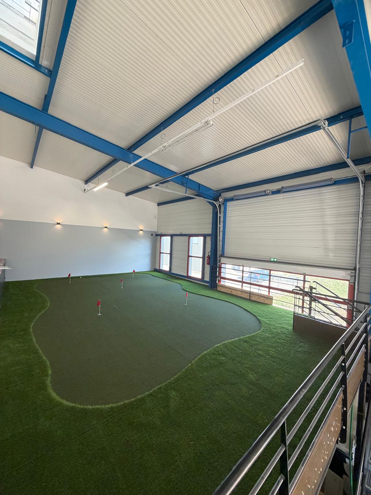 Putting green indoor du Golf Lab de Douvaine avec drapeaux rouges et structure métallique